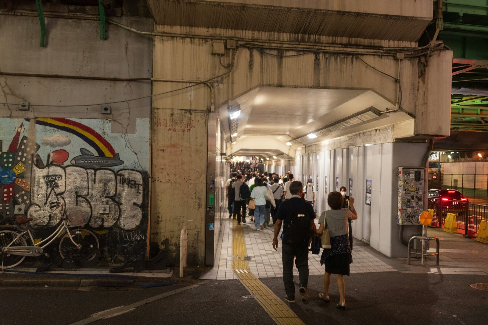 A group of people walking down a street next to a graffiti covered wall